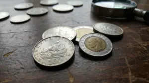 Monete da 500 lire d'argento italiane su un tavolo di legno accanto a una lente d'ingrandimento