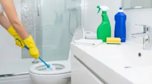 Persona con guanti gialli che pulisce il WC in un bagno moderno con prodotti per la pulizia