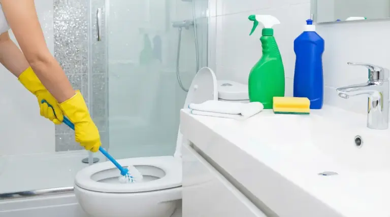 Persona con guanti gialli che pulisce il WC in un bagno moderno con prodotti per la pulizia
